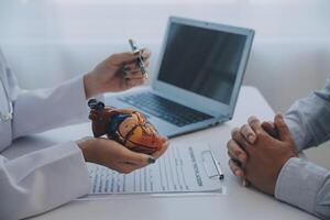 Doctor explaining heart to elderly patient. Doctor explaining the heart model. Doctors pen point to a model of the heart photo