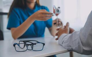 Close-up of Asian female doctor talking with elderly patient showing eyeball model and explaining eye disease in hospital photo