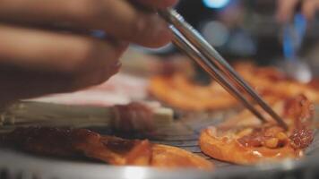 dichtbij omhoog schot van hand- Koken Koreaans gegrild varkensvlees buik vlees en gebruik schaar naar besnoeiing vlees Aan ijzer rooster pan.varkensvlees buik Aan een grill, samgyupsal, koken varkensvlees buik Aan een pan, koreaans varkensvlees barbecue video