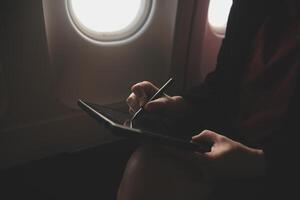 Blonde female tourist checking incoming notification on smartphone sitting on seat of airplane with netbook.Young businesswoman share media from telephone on laptop computer during plane flight photo