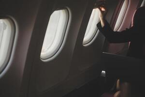 Blonde female tourist checking incoming notification on smartphone sitting on seat of airplane with netbook.Young businesswoman share media from telephone on laptop computer during plane flight photo