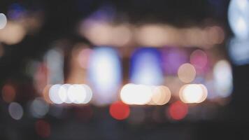 schön Bokeh im ein dunkel verschwommen Hintergrund beim Nacht auf das Gehen Straße mit das Personen. das runden bunt Bokeh scheinen von Gebäude und Geschäfte im das Stadt Lebensstil. abstrakt Konzept. video