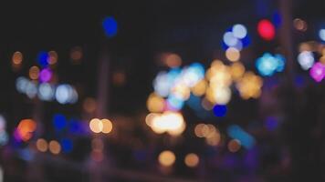 bellissimo bokeh nel un' buio sfocato sfondo a notte su il a piedi strada con il le persone. il il giro colorato bokeh brillare a partire dal edifici e negozi nel il città stile di vita. astratto concetto. video