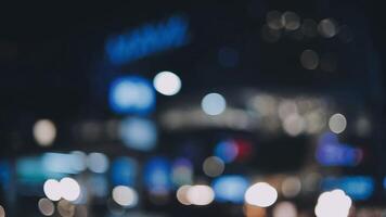 bellissimo bokeh nel un' buio sfocato sfondo a notte su il a piedi strada con il le persone. il il giro colorato bokeh brillare a partire dal edifici e negozi nel il città stile di vita. astratto concetto. video