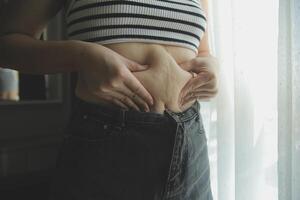 mujer cuerpo grasa barriga. obeso mujer mano participación excesivo barriga gordo. dieta estilo de vida concepto a reducir barriga y forma arriba sano estómago músculo. foto