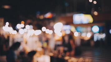 bellissimo bokeh nel un' buio sfocato sfondo a notte su il a piedi strada con il le persone. il il giro colorato bokeh brillare a partire dal edifici e negozi nel il città stile di vita. astratto concetto. video