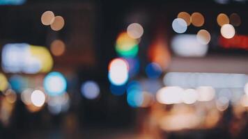 bellissimo bokeh nel un' buio sfocato sfondo a notte su il a piedi strada con il le persone. il il giro colorato bokeh brillare a partire dal edifici e negozi nel il città stile di vita. astratto concetto. video