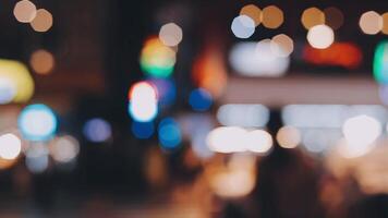 mooi bokeh in een donker wazig achtergrond Bij nacht Aan de wandelen straat met de mensen. de ronde kleurrijk bokeh schijnen van gebouwen en winkels in de stad levensstijl. abstract concept. video