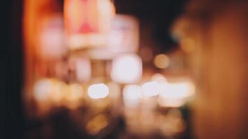 bellissimo bokeh nel un' buio sfocato sfondo a notte su il a piedi strada con il le persone. il il giro colorato bokeh brillare a partire dal edifici e negozi nel il città stile di vita. astratto concetto. video