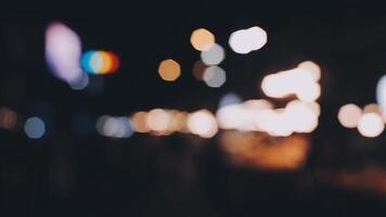 bellissimo bokeh nel un' buio sfocato sfondo a notte su il a piedi strada con il le persone. il il giro colorato bokeh brillare a partire dal edifici e negozi nel il città stile di vita. astratto concetto. video