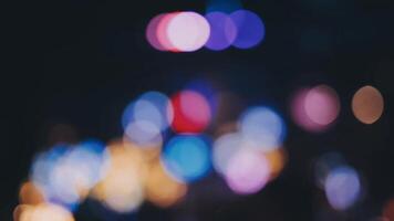 bellissimo bokeh nel un' buio sfocato sfondo a notte su il a piedi strada con il le persone. il il giro colorato bokeh brillare a partire dal edifici e negozi nel il città stile di vita. astratto concetto. video