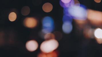 bellissimo bokeh nel un' buio sfocato sfondo a notte su il a piedi strada con il le persone. il il giro colorato bokeh brillare a partire dal edifici e negozi nel il città stile di vita. astratto concetto. video