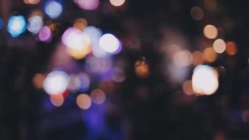 bellissimo bokeh nel un' buio sfocato sfondo a notte su il a piedi strada con il le persone. il il giro colorato bokeh brillare a partire dal edifici e negozi nel il città stile di vita. astratto concetto. video