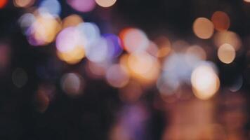 bellissimo bokeh nel un' buio sfocato sfondo a notte su il a piedi strada con il le persone. il il giro colorato bokeh brillare a partire dal edifici e negozi nel il città stile di vita. astratto concetto. video