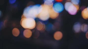 bellissimo bokeh nel un' buio sfocato sfondo a notte su il a piedi strada con il le persone. il il giro colorato bokeh brillare a partire dal edifici e negozi nel il città stile di vita. astratto concetto. video