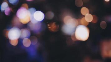 bellissimo bokeh nel un' buio sfocato sfondo a notte su il a piedi strada con il le persone. il il giro colorato bokeh brillare a partire dal edifici e negozi nel il città stile di vita. astratto concetto. video