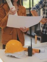 masculino y hembra industrial ingenieros en difícil sombreros discutir nuevo proyecto mientras utilizando ordenador portátil. ellos hacer demostración gestos ellos trabajo en un pesado industria fabricación fábrica. foto