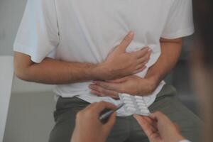 Man suffering with severe stomach pain sitting at home. Hand of mature guy holding abdomen suffering from ache, diarrhea or indigestive problem. Caucasian guy pressing on belly on painful sensation photo