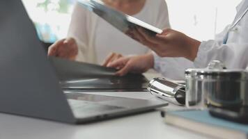 grave femmina medico utilizzando il computer portatile e scrittura Appunti nel medico rivista seduta a scrivania. giovane donna professionale medico medico indossare bianca cappotto e stetoscopio Lavorando su computer a posto di lavoro. video