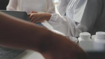 sérieux femelle médecin en utilisant portable et l'écriture Remarques dans médical journal séance à bureau. Jeune femme professionnel médical médecin portant blanc manteau et stéthoscope travail sur ordinateur à lieu de travail. video