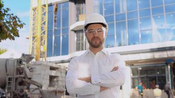ein Ingenieur im ein Weiß Hemd und Helm steht gegen das Hintergrund von ein modern Glas Gebäude. modern Konstruktion video
