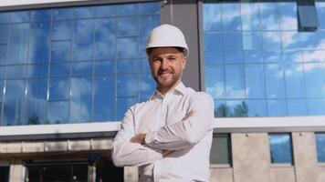 un ingénieur dans une blanc chemise et casque des stands contre le toile de fond de une moderne verre bâtiment. moderne construction video