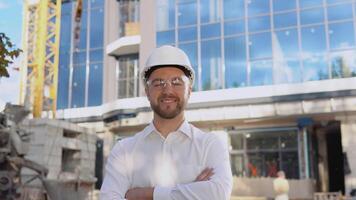 un ingeniero en un blanco camisa y casco soportes en contra el fondo de un moderno vaso edificio video