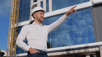 Engineer architect in a white shirt and helmet on the background of a modern glass building manages the construction process video