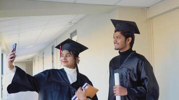 Two Indian graduates stand in a university hallway and take a selfie video