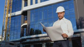 arquitecto ingeniero lee proyecto dibujos. un ingeniero en un blanco camisa y casco trabajos en el construcción de un moderno vaso edificio video