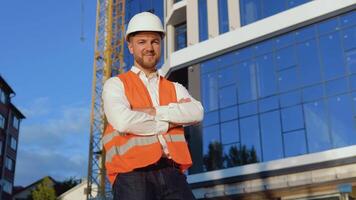 a engenheiro-arquiteto dentro uma branco camisa, capacete e laranja trabalhos colete carrinhos contra a pano de fundo do uma moderno vidro construção video