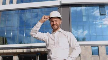 een ingenieur in een wit overhemd en helm staat tegen de backdrop van een modern glas gebouw. modern bouw video