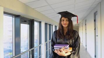 indiano fêmea graduado dentro manto carrinhos com uma livros dentro dela mãos e sorrisos video