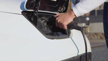 A male driver connects electric car to power system to charge car battery video