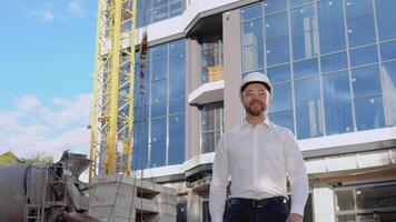 An engineer in a white shirt and helmet stands against the backdrop of a modern glass building. Modern construction video