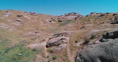 The drone flies over rocky hills surrounded by mountains on a cloudless day video