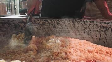 The chef stirs steaming rice in a large pilaf cauldron with a slotted spoon video