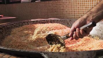 The chef stirs steaming rice in a large pilaf cauldron with a slotted spoon video