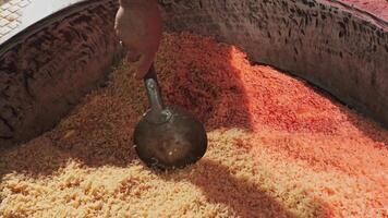 The chef stirs steaming rice in a large pilaf cauldron with a slotted spoon video