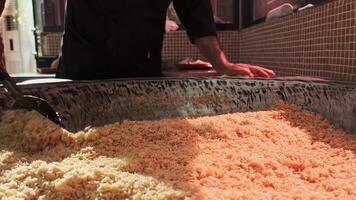 The chef stirs steaming rice in a large pilaf cauldron with a slotted spoon video