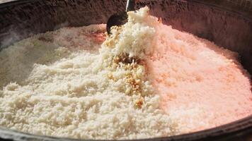 The chef stirs steaming rice in a large pilaf cauldron with a slotted spoon video