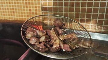 The chef puts pieces of meat with a slotted spoon into the oil boiling in a large pilaf cauldron video