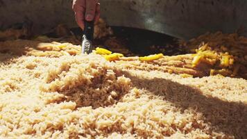 The chef puts rice with a slotted spoon into plates from a large cauldron for pilaf video