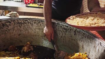 The chef puts carrots with a slotted spoon in a plate with rice from a large cauldron for pilaf video