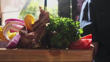 a chefe de cozinha demonstra uma de madeira borda servido com cozinhou carne, cebolas, ervas, tomates e legumes video