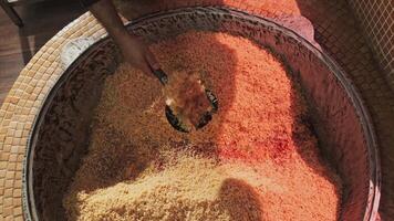 The chef tosses rice with a slotted spoon in a large cauldron while cooking pilaf video