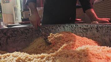 el cocinero lanzamientos arroz con un ranurado cuchara en un grande caldera mientras Cocinando pilaf video