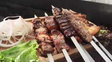 A waiter demonstrates a wooden tray with chicken, meat and liver kebabs, served with onions, herbs and vegetables. video