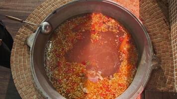 Chef mixes meat soup with vegetables in a large cauldron with a slotted spoon video