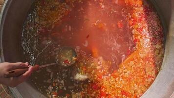 Chef mixes meat soup with vegetables in a large cauldron with a slotted spoon video